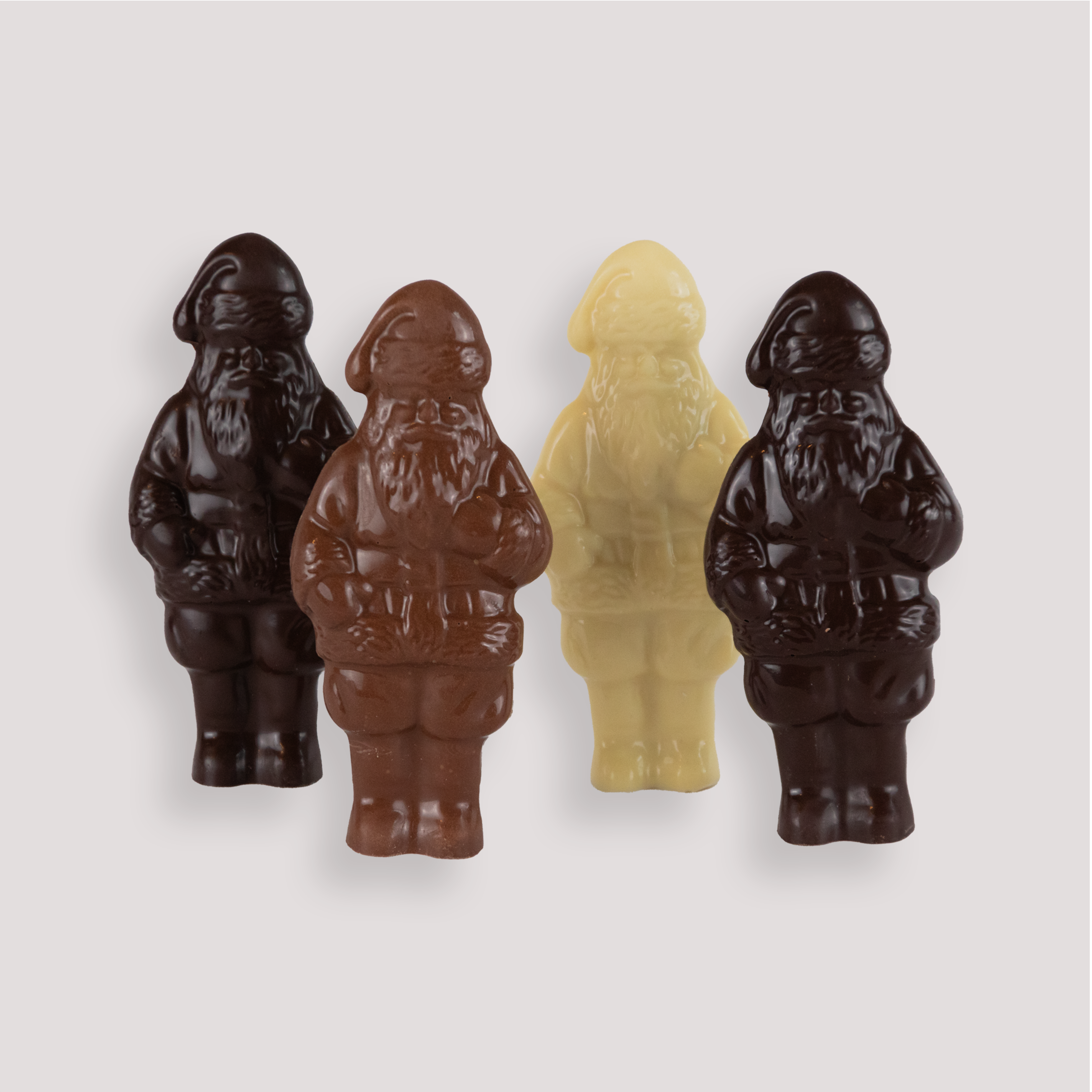 Four unwrapped solid chocolate Santas made with four different types of chocolate, standing upright in a white fluted bowl, crafted by Saratoga Chocolate Co.