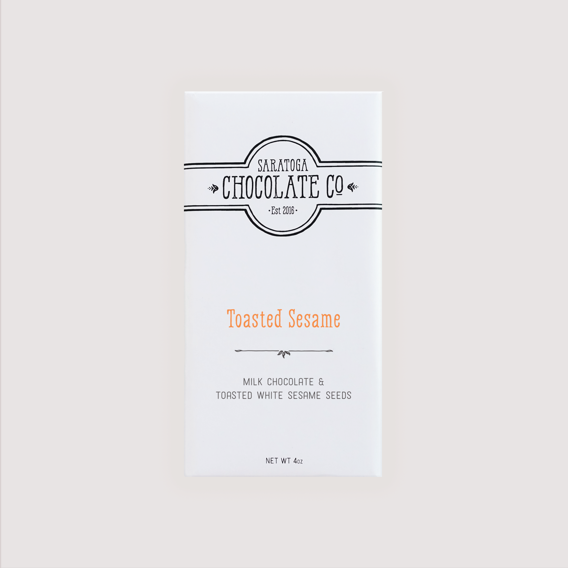 Front of Saratoga Chocolate Co. Toasted Sesame Bar wrapped in a white paper package with a Blue flavor label. Label features the Saratoga Chocolate Co. logo and describes the bar as milk chocolate and toasted white sesame seeds. This bar is gluten free.