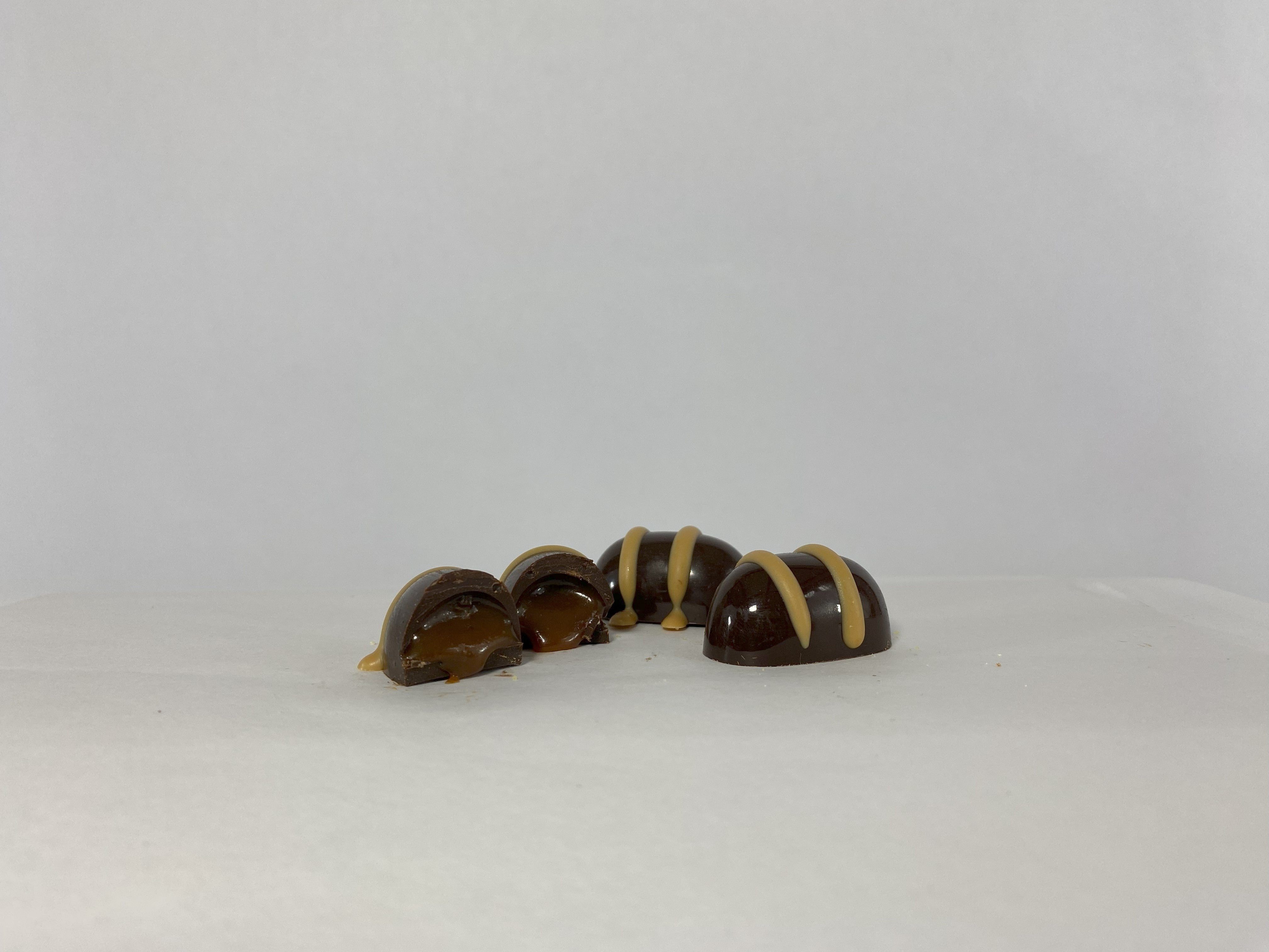 Close-up of a Saratoga Chocolate Co. Salted Caramel Truffle sliced open, revealing a luscious, golden caramel filling infused with fleur de sel, encased in a rich dark chocolate shell and topped with a delicate drizzle of salted caramel chocolate.