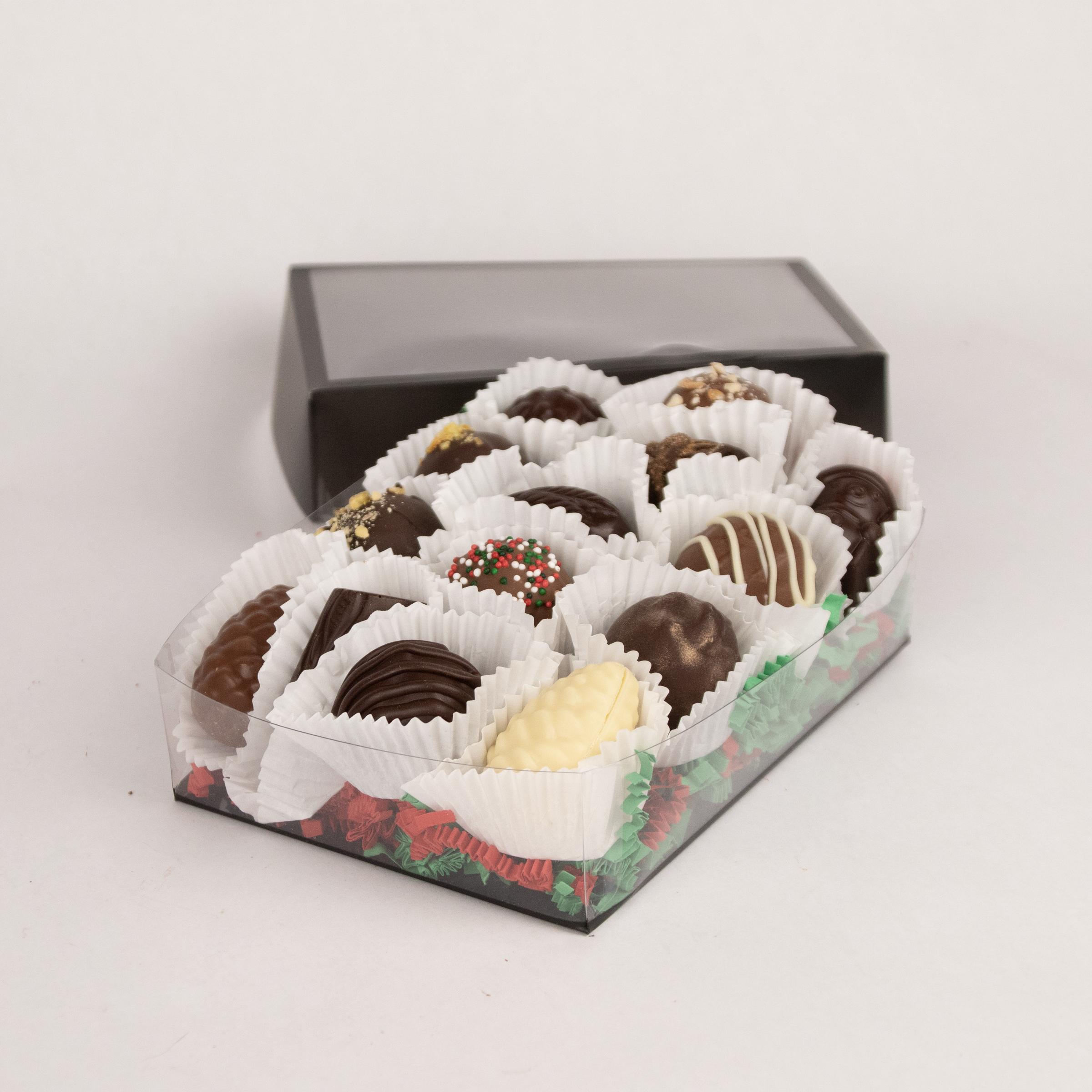 Saratoga Chocolate Co holiday collection of 12 assorted truffles, beautifully arranged in a black box with a clear top, showcasing a variety of festive designs and flavors.