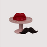 Bright Red oversized wax lips, and a black wax handlebar moustache displayed on a small pink pedestal plate. 