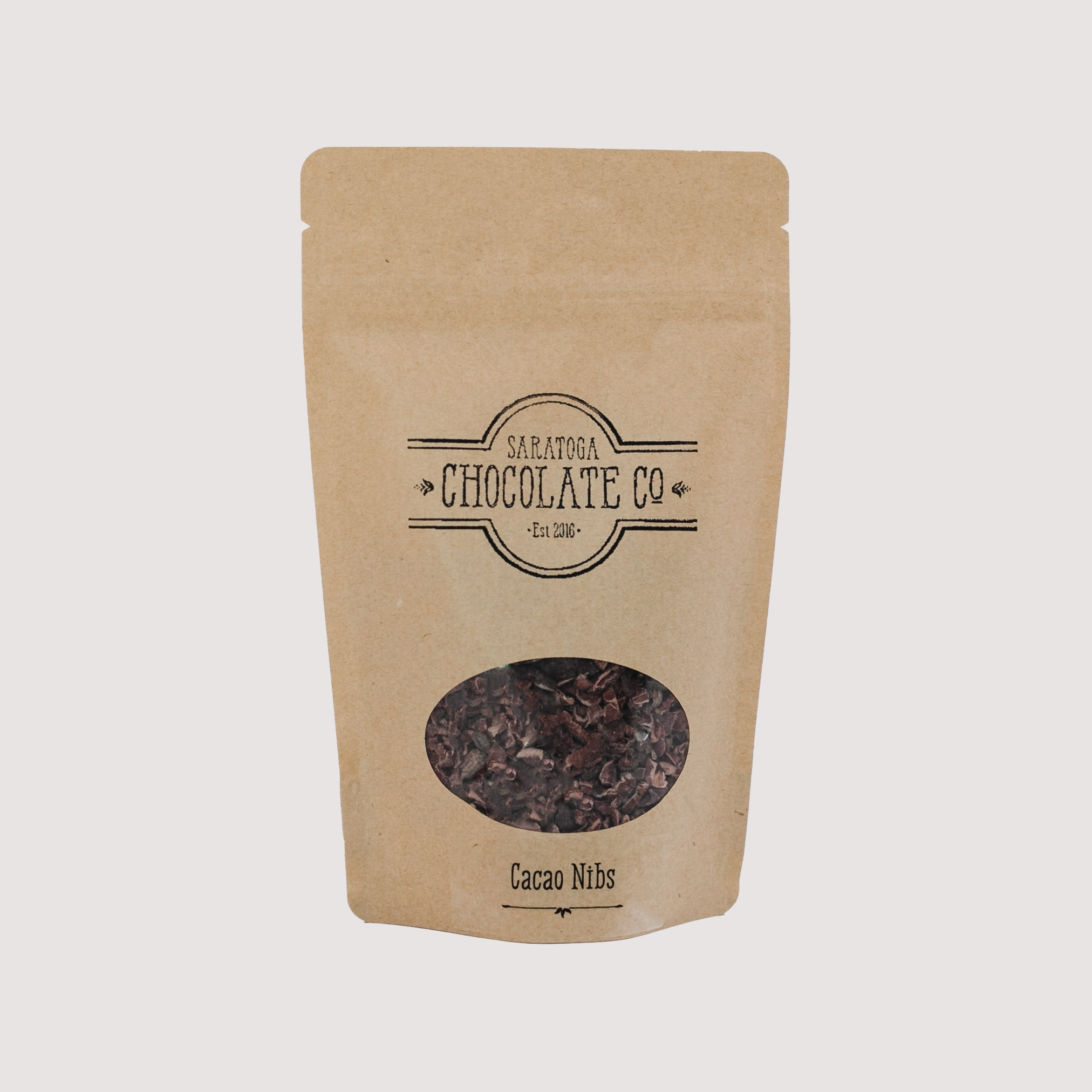 One brown resealable bag of Saratoga Chocolate Co. Cacao Nibs with a clear round window showing the product inside, placed against a light background.