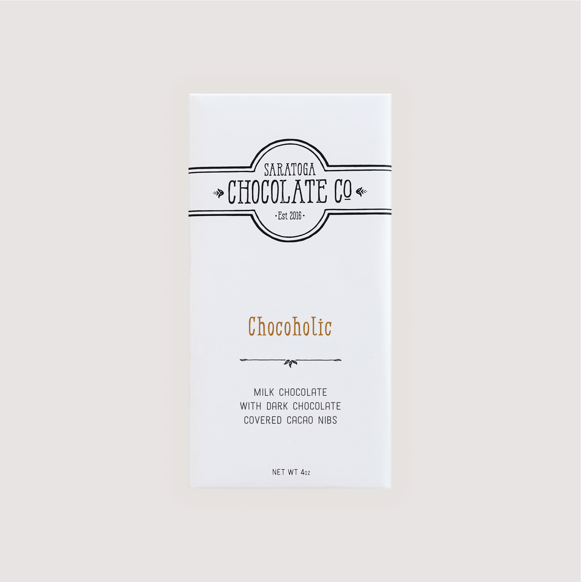 Wrapped Saratoga Chocolate Co. Chocoholic Bar in a white paper package with a brown flavor label. Label features the black Saratoga Chocolate Co. logo and describes the bar as creamy milk chocolate with dark chocolate-covered cacao nibs. This bar is gluten free.
