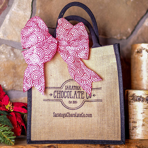 A tote bag with Saratoga Chocolate Co logo and red and white pattern ribbon.  