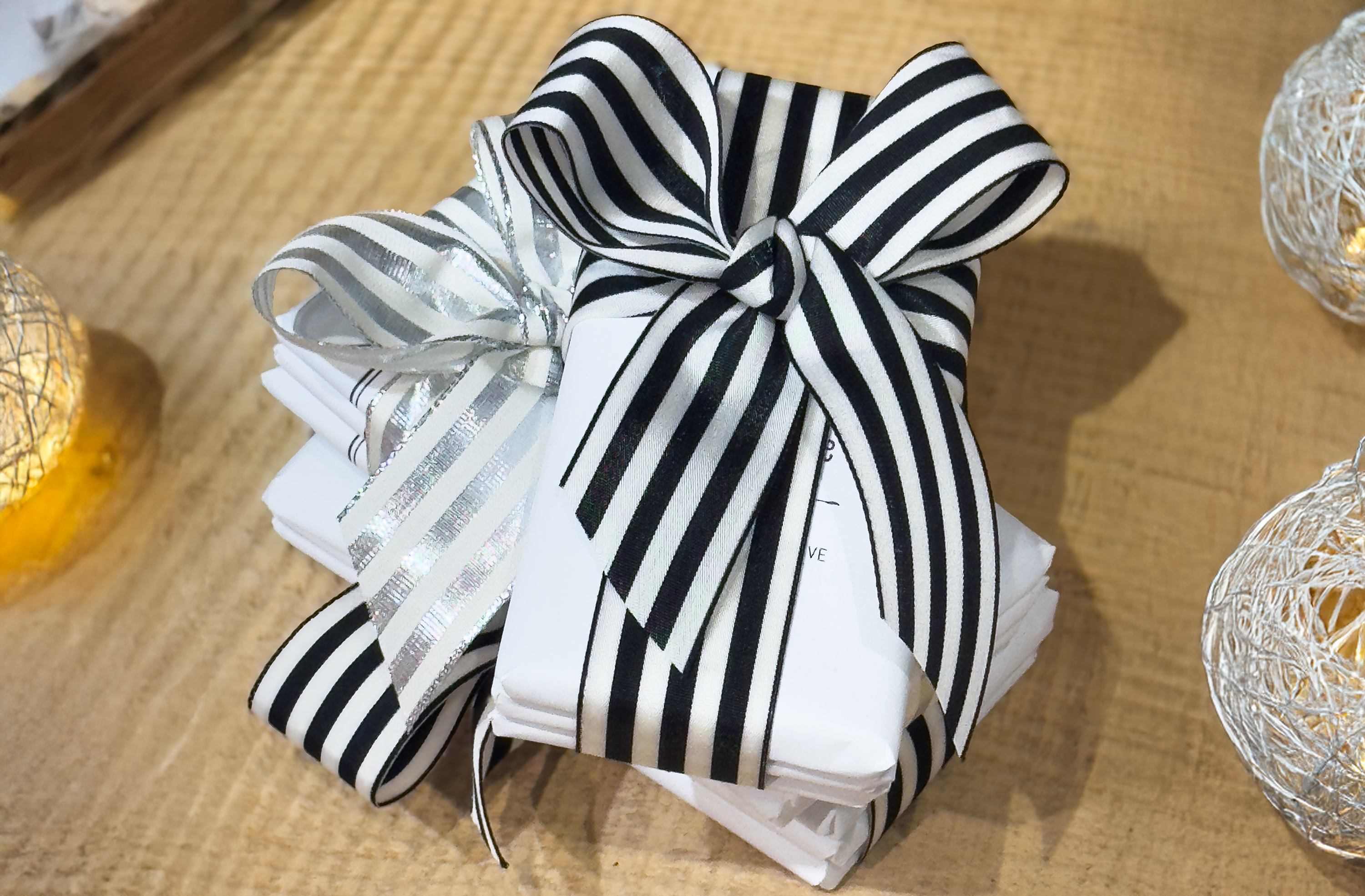 White stack of white wrapped chocolate bars made by Saratoga Chocolate Co with black and white striped bow for gift  purpose. All displayed on a wooden surface